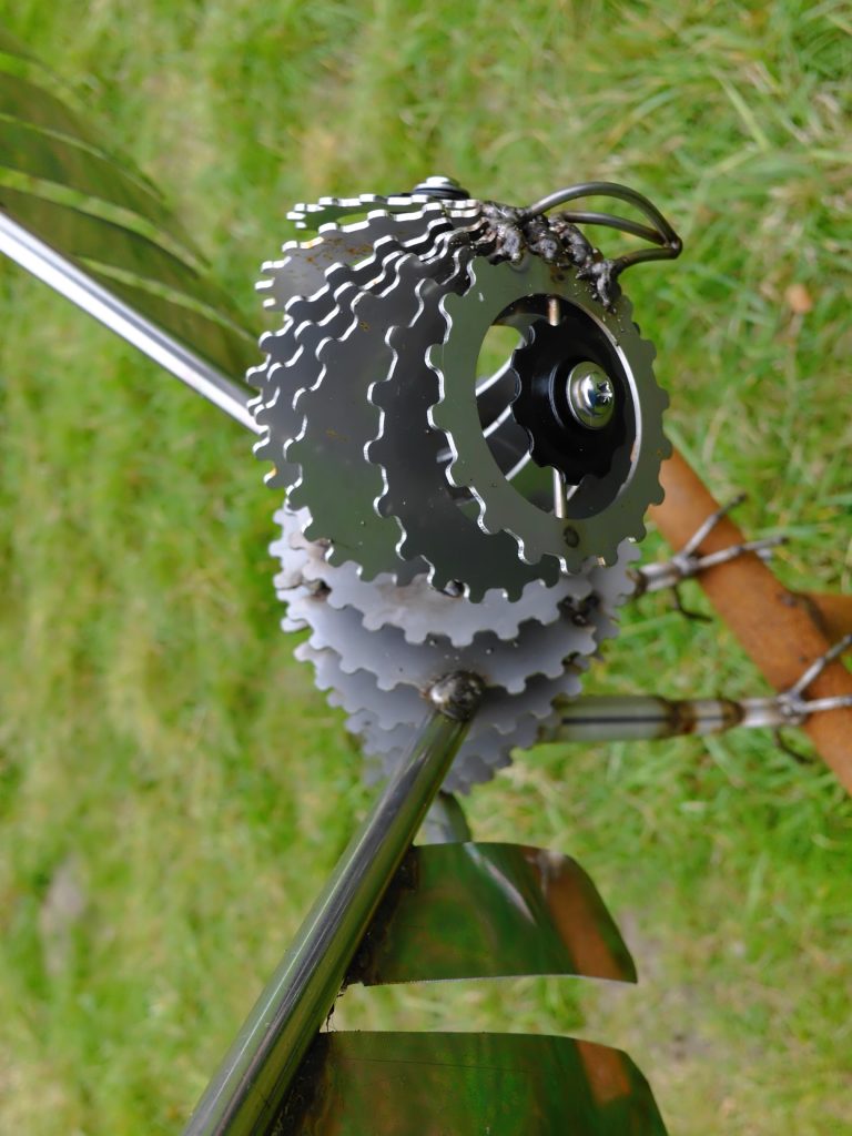 Close-up of a bicycle gear cassette attached to a metal sculpture on green grass.
