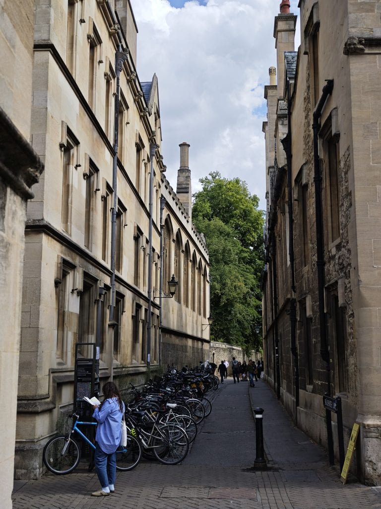 A woman stands near parked bicycles along a narrow alley between old stone buildings on a cloudy day.