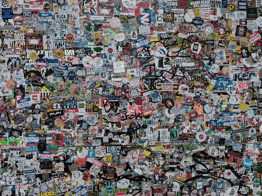 A wall densely covered with a variety of colorful stickers, logos, and graffiti in different languages and styles.