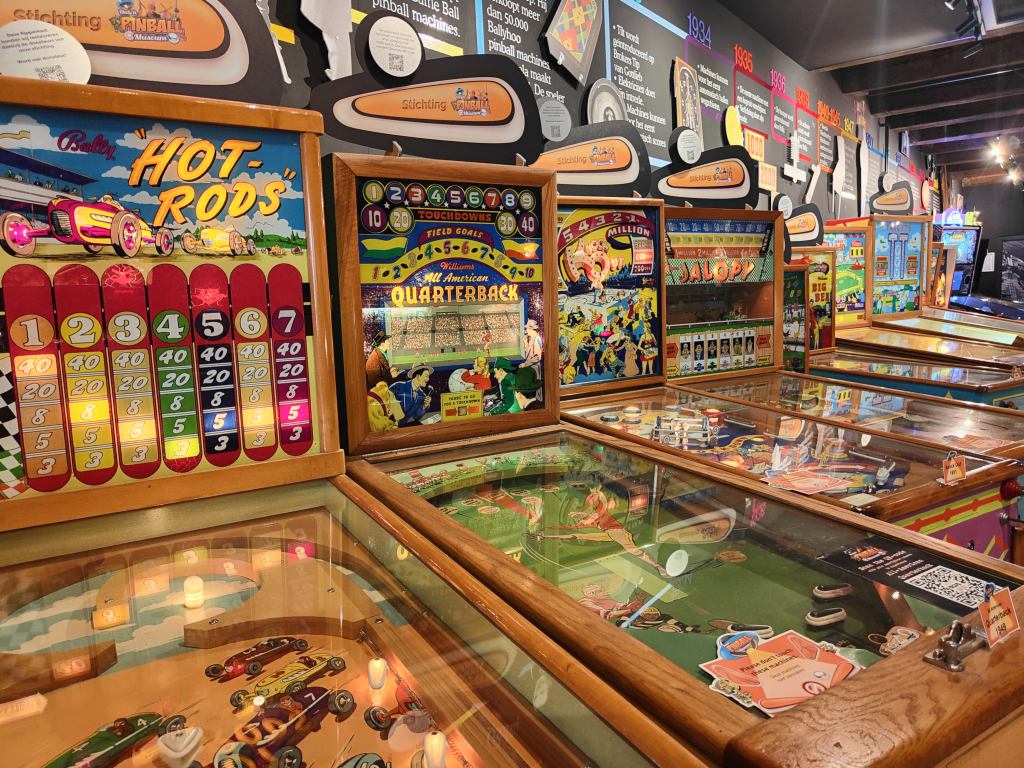 Row of vintage pinball machines with colorful artwork and themed playfields in a game arcade.