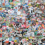 A wall densely covered with colorful stickers, featuring various logos, drawings, and text in different styles and sizes.