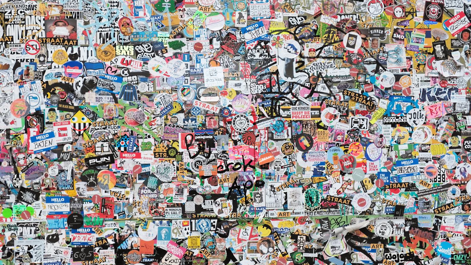 A wall densely covered with colorful stickers, featuring various logos, drawings, and text in different styles and sizes.