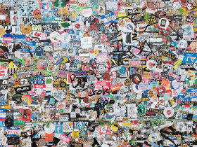 A wall densely covered with colorful stickers, featuring various logos, drawings, and text in different styles and sizes.