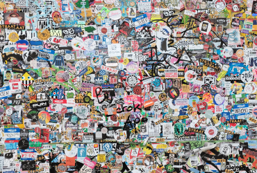 A wall densely covered with colorful stickers, featuring various logos, drawings, and text in different styles and sizes.