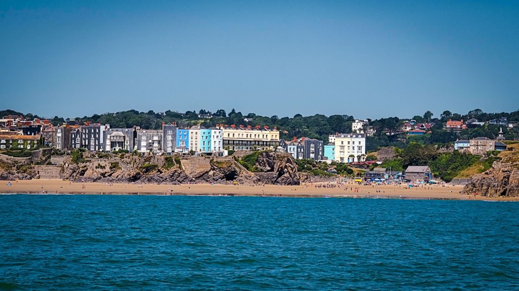 Colorful buildings line a beach above sand and rocky cliffs, with people visible and water in the foreground.