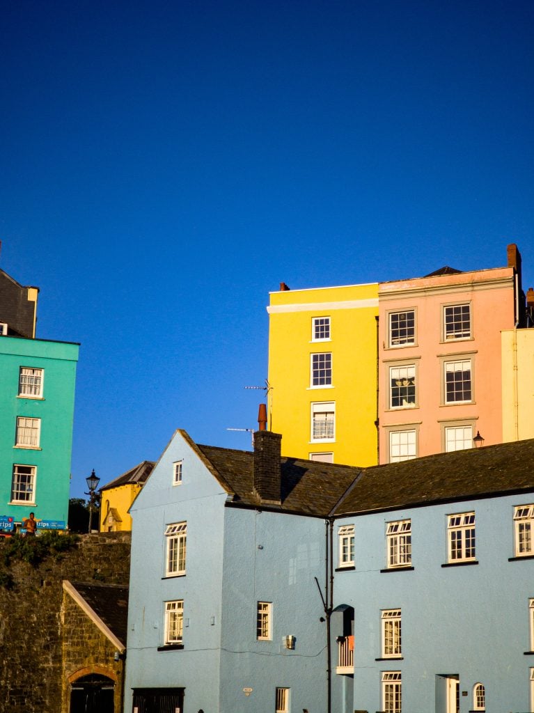 Colorful pastel buildings under a clear blue sky with sunlight illuminating the facades.
