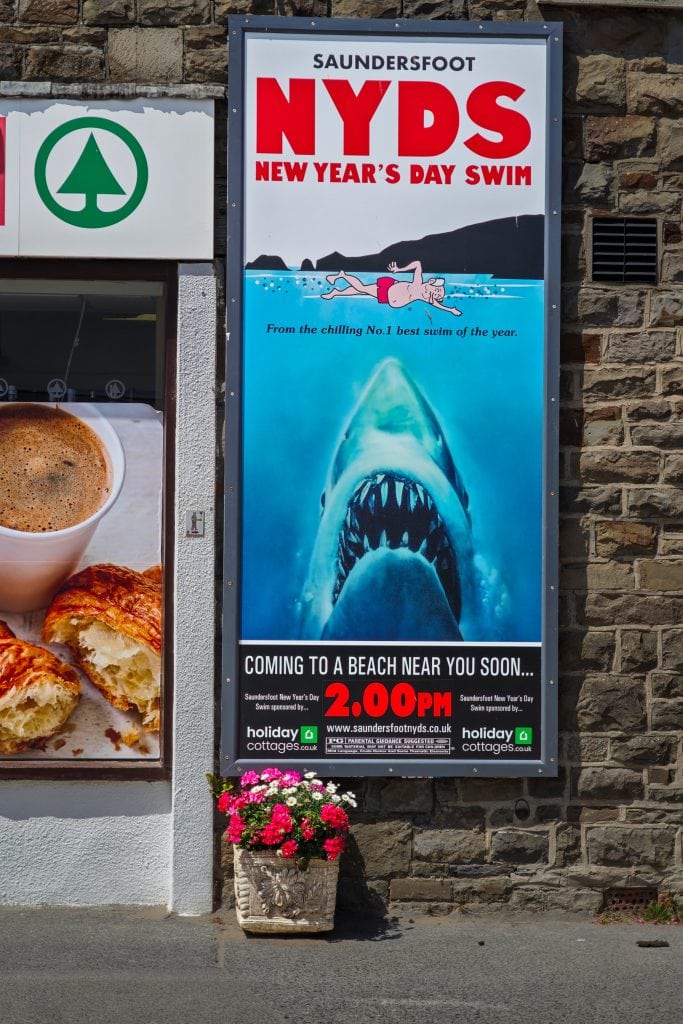 Poster for Saundersfoot NYDS New Year’s Day Swim featuring a cartoon swimmer and a shark under the water.